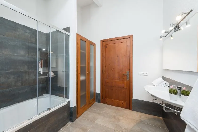 Un baño con ducha de cristal, puertas de madera y un lavabo blanco.