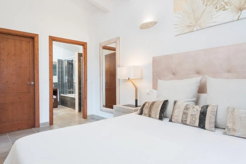 Un dormitorio luminoso con cama, cabecero tapizado y lámpara de noche.