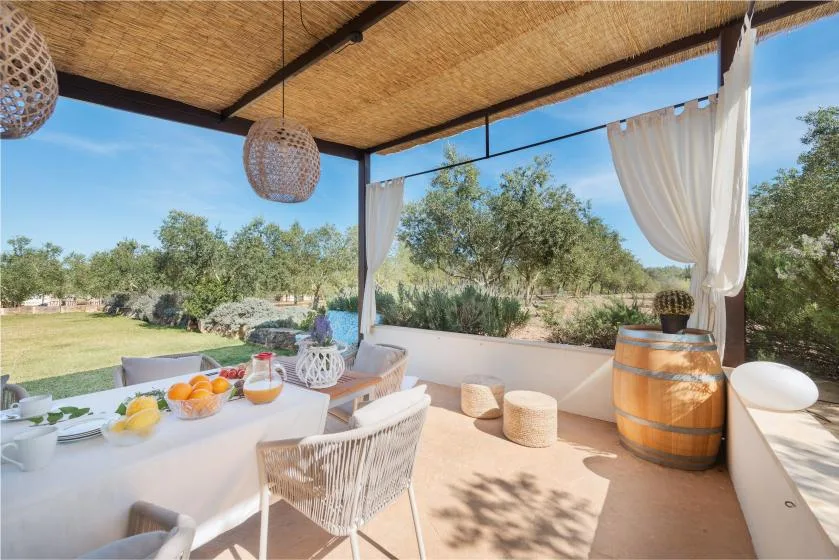 Un comedor exterior a la sombra da a un jardín, con una mesa preparada para comer.