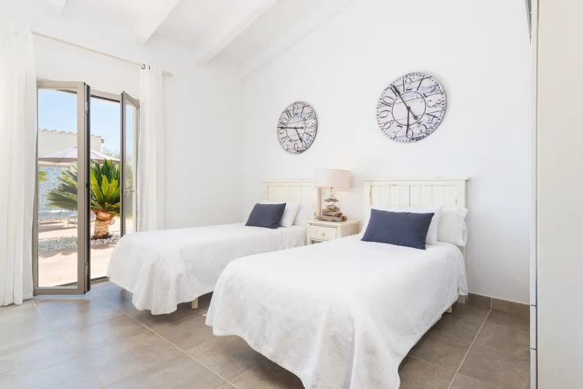 Un dormitorio luminoso con dos camas y grandes relojes decorativos en la pared.