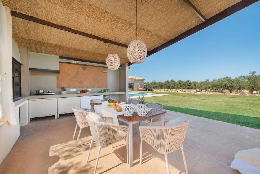Comedor exterior cubierto con una mesa junto a una cocina abierta y un césped.