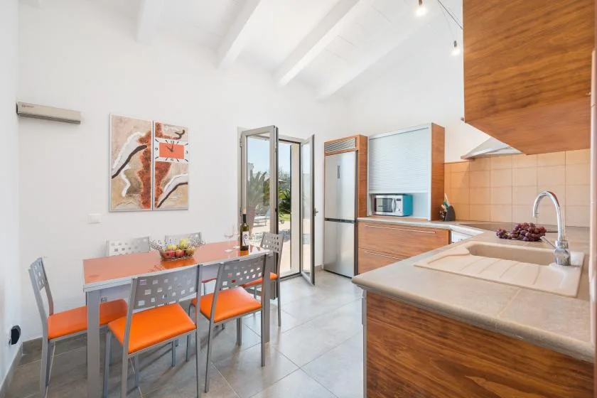 Una cocina luminosa con zona de comedor, asientos naranjas y una puerta de vidrio abierta.
