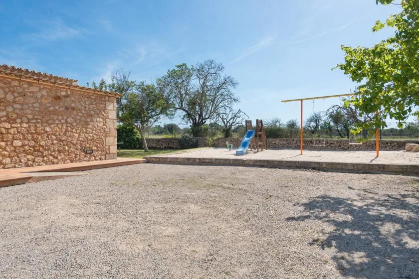 Un parque infantil al aire libre con un tobogán y columpios sobre una superficie de grava.