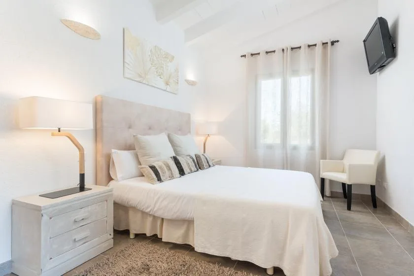 Un dormitorio luminoso con una cama bien arreglada, mesillas y una ventana con cortinas.