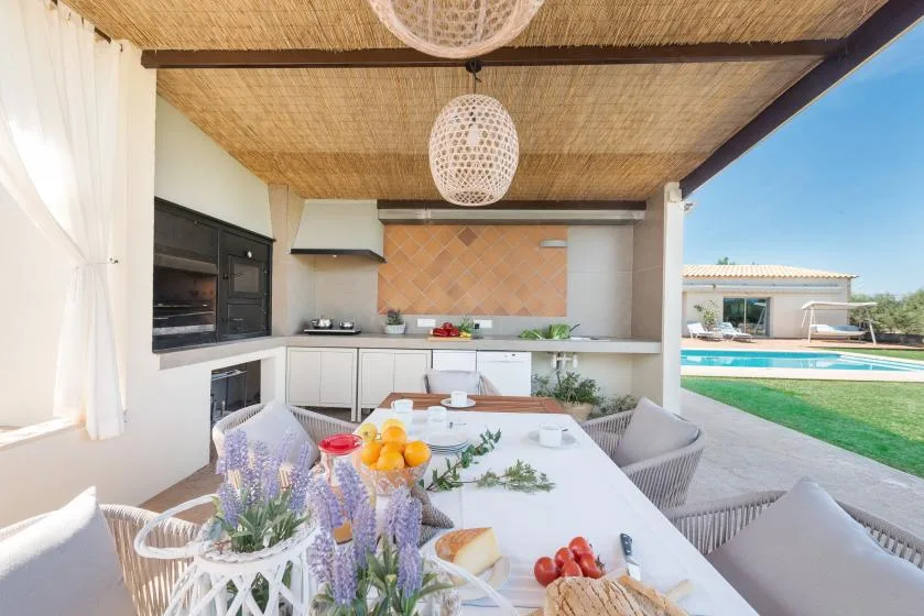 Comedor al aire libre junto a una cocina, con una mesa bajo un patio cubierto.