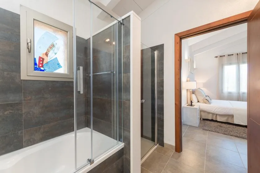 Un baño con una ducha de vidrio junto a una puerta abierta que da a un dormitorio.