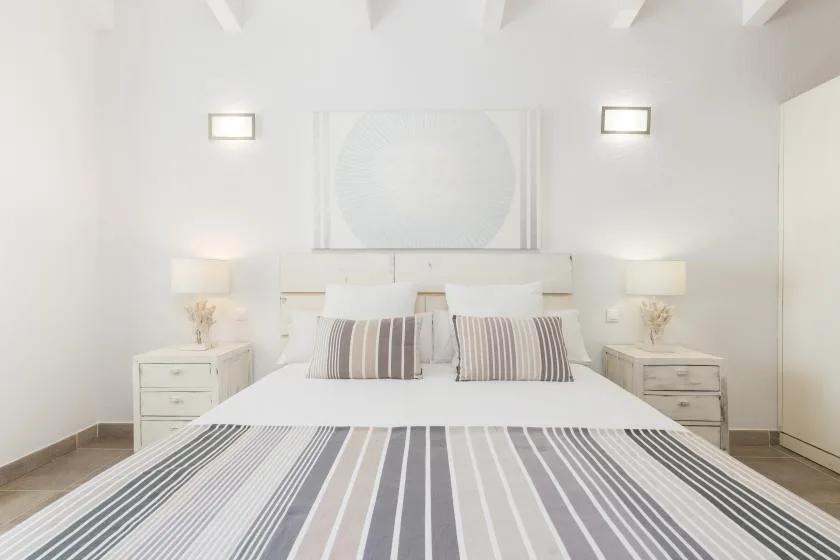 Un dormitorio luminoso con una cama vestida con ropa de cama a rayas y mesitas de noche a juego.
