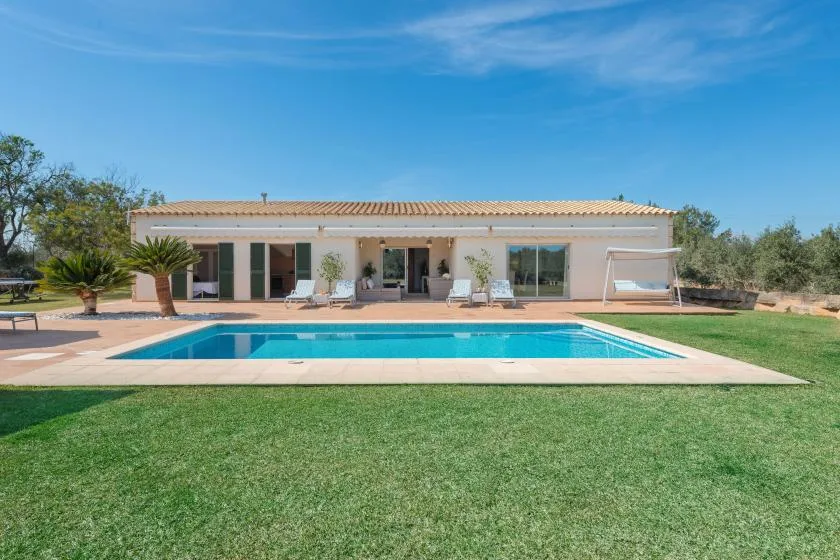 Una casa y una piscina se encuentran detrás de un césped bajo un cielo azul despejado.