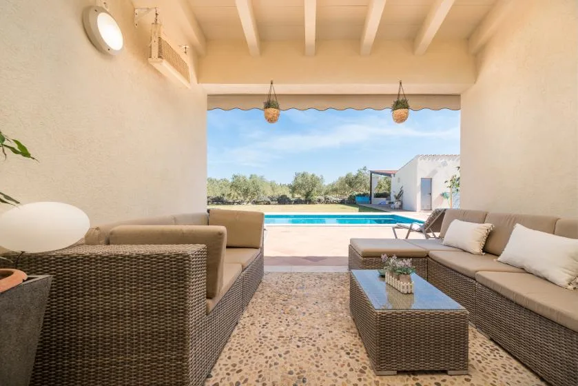 Una zona de estar exterior cubierta da a una piscina y un paisaje abierto.