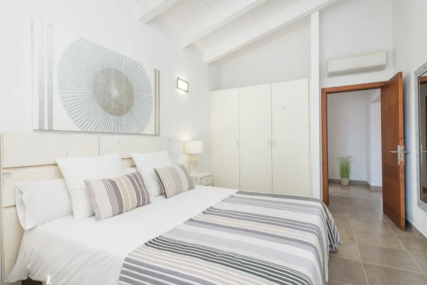 Un dormitorio luminoso con ropa de cama blanca y una colcha de rayas grises.