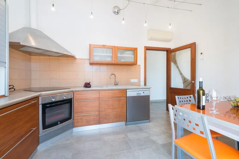 Una cocina luminosa con gabinetes de madera, electrodomésticos de acero inoxidable y una mesa de comedor.