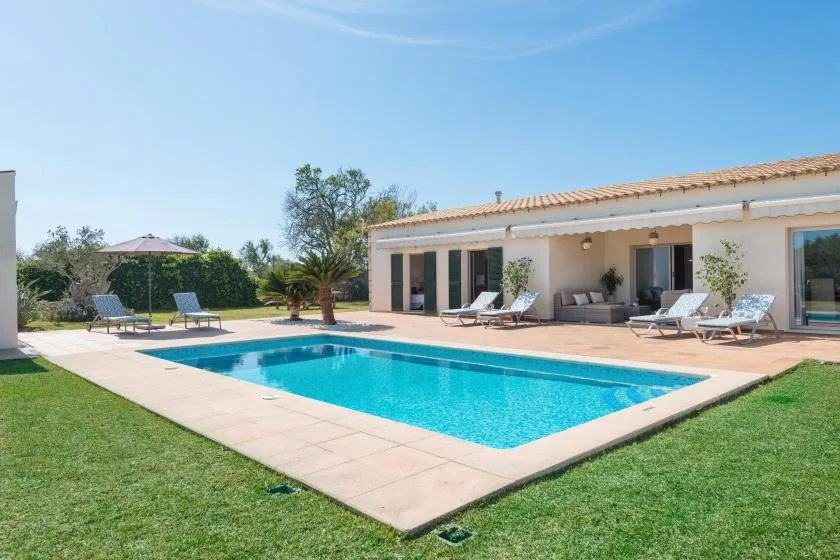 Una piscina y asientos en el patio están junto a una casa de una planta.