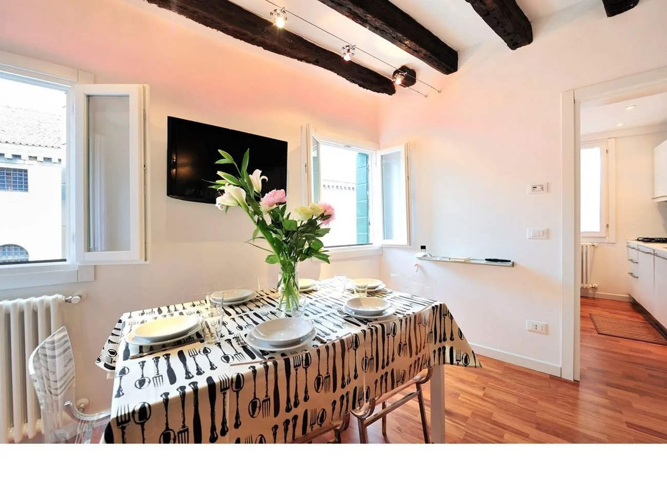 A dining area with a set table and a vase of flowers beneath exposed ceiling beams.