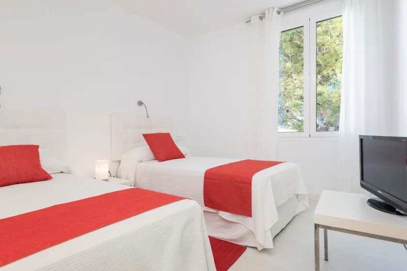 Un dormitorio luminoso con dos camas vestidas con ropa de cama blanca y roja.
