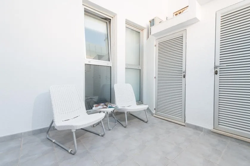 Un patio luminoso con suelo de baldosas, asientos blancos y puertas con persianas.