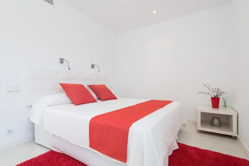 Un dormitorio luminoso con ropa de cama blanca y detalles rojos.