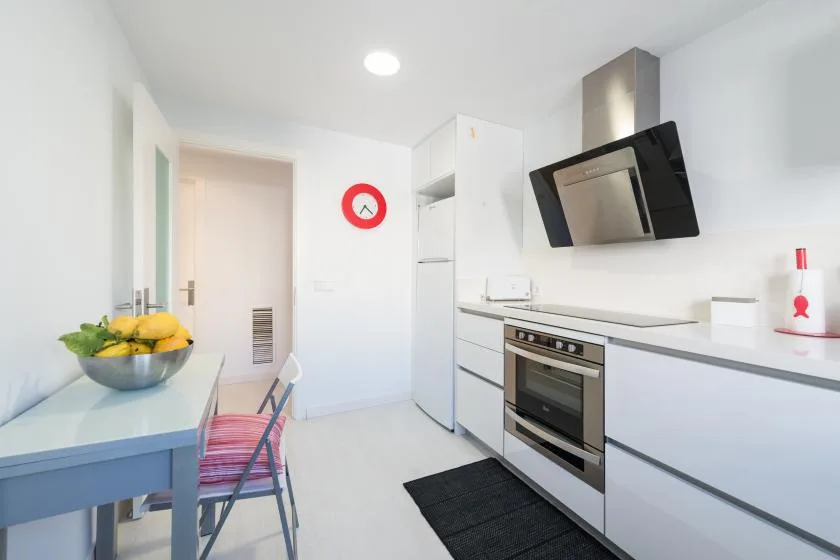Una cocina luminosa con gabinetes blancos, horno y una pequeña mesa de comedor.