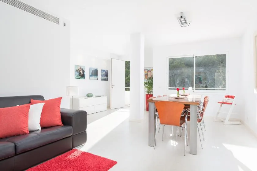 Una luminosa sala de estar y comedor con un sofá oscuro y una mesa junto a la ventana.