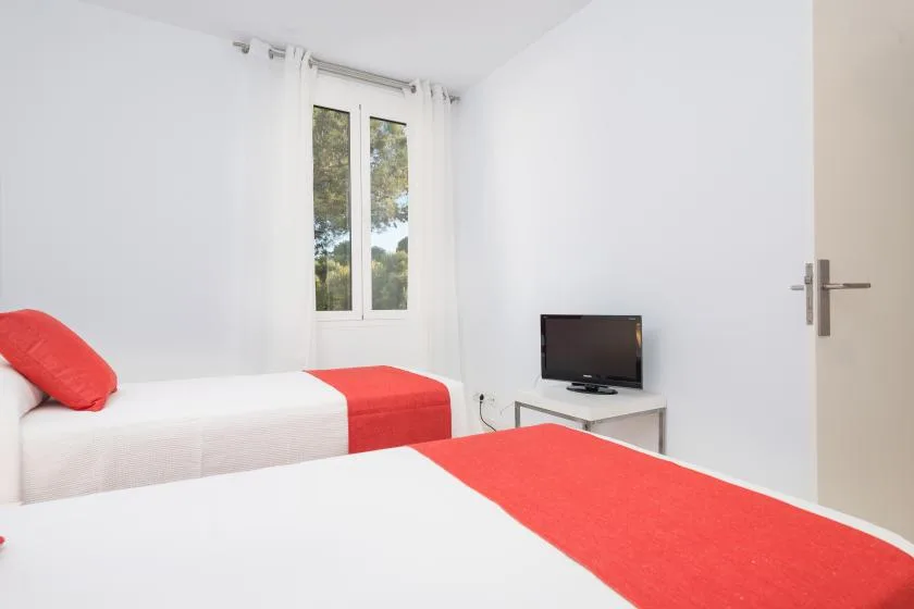 Un dormitorio luminoso con dos camas vestidas con ropa de cama blanca y roja.