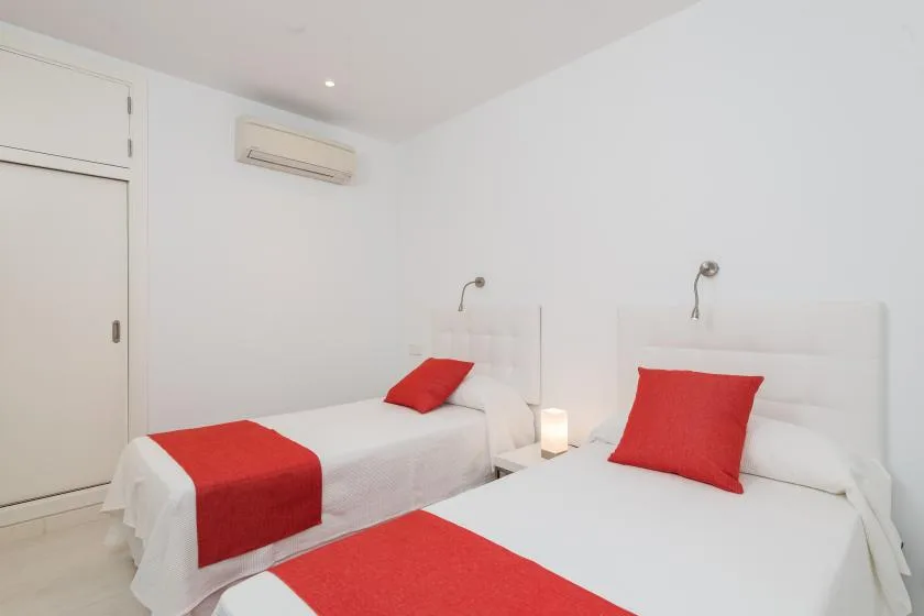 Un dormitorio luminoso con dos camas vestidas con ropa de cama blanca y roja.