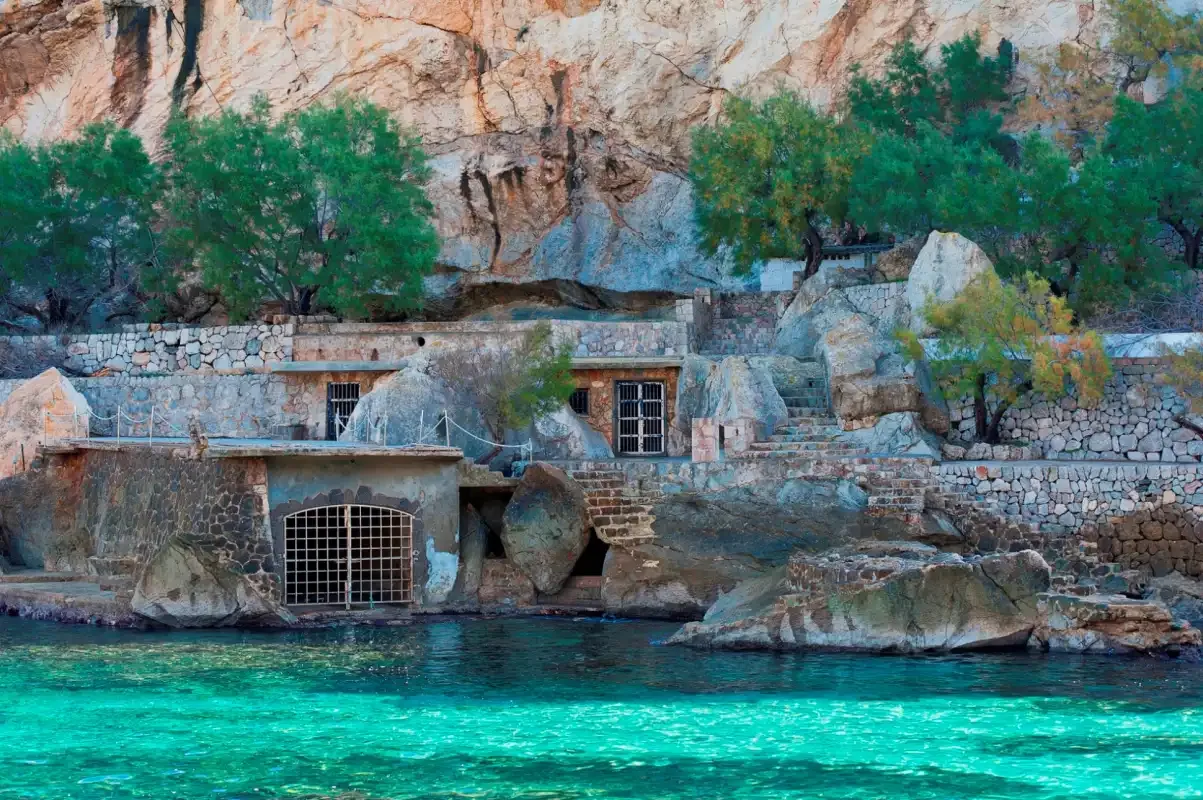 Una escena rocosa junto al agua, con edificios de piedra y aguas turquesas.