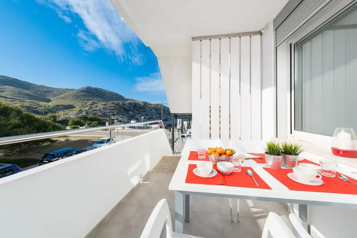 Comedor en un balcón con la mesa puesta y vistas a colinas verdes.