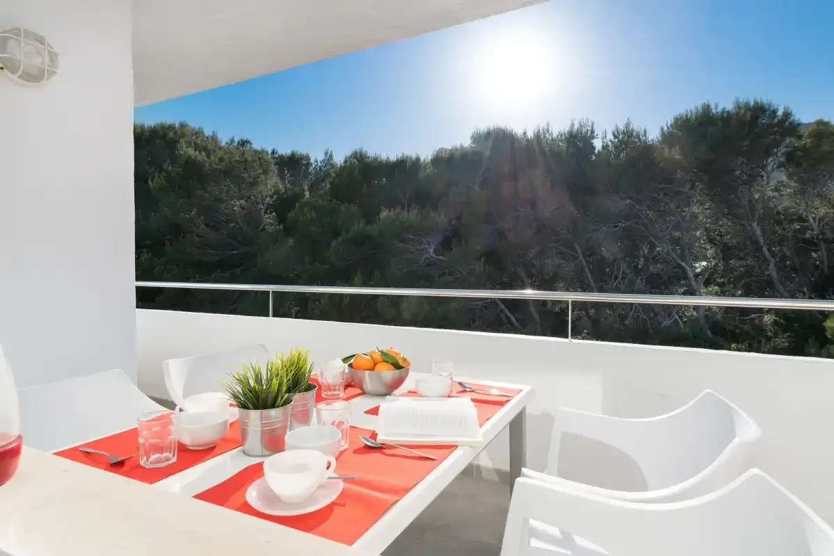 Una luminosa zona de comedor al aire libre con una mesa puesta frente a árboles verdes.