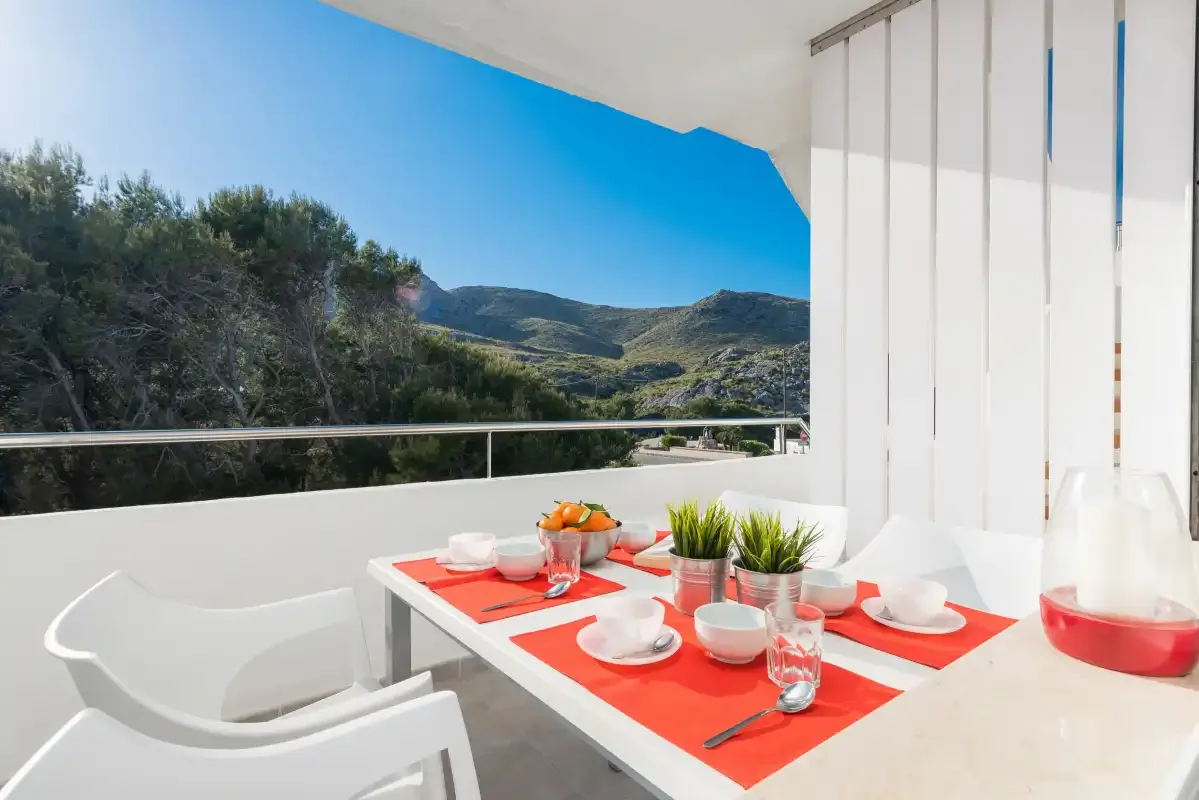 Una mesa de comedor en una terraza tiene vistas a colinas verdes bajo un cielo despejado.