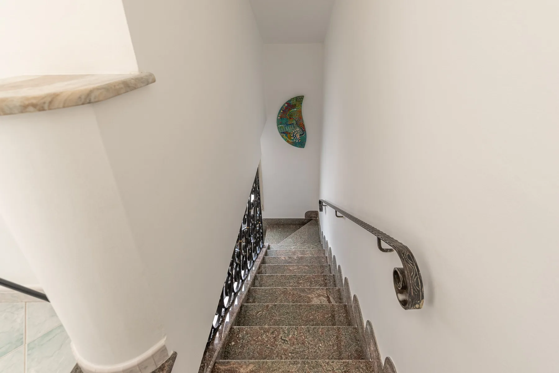 Una escalera interior estrecha desciende entre paredes blancas, con pasamanos metálicos.