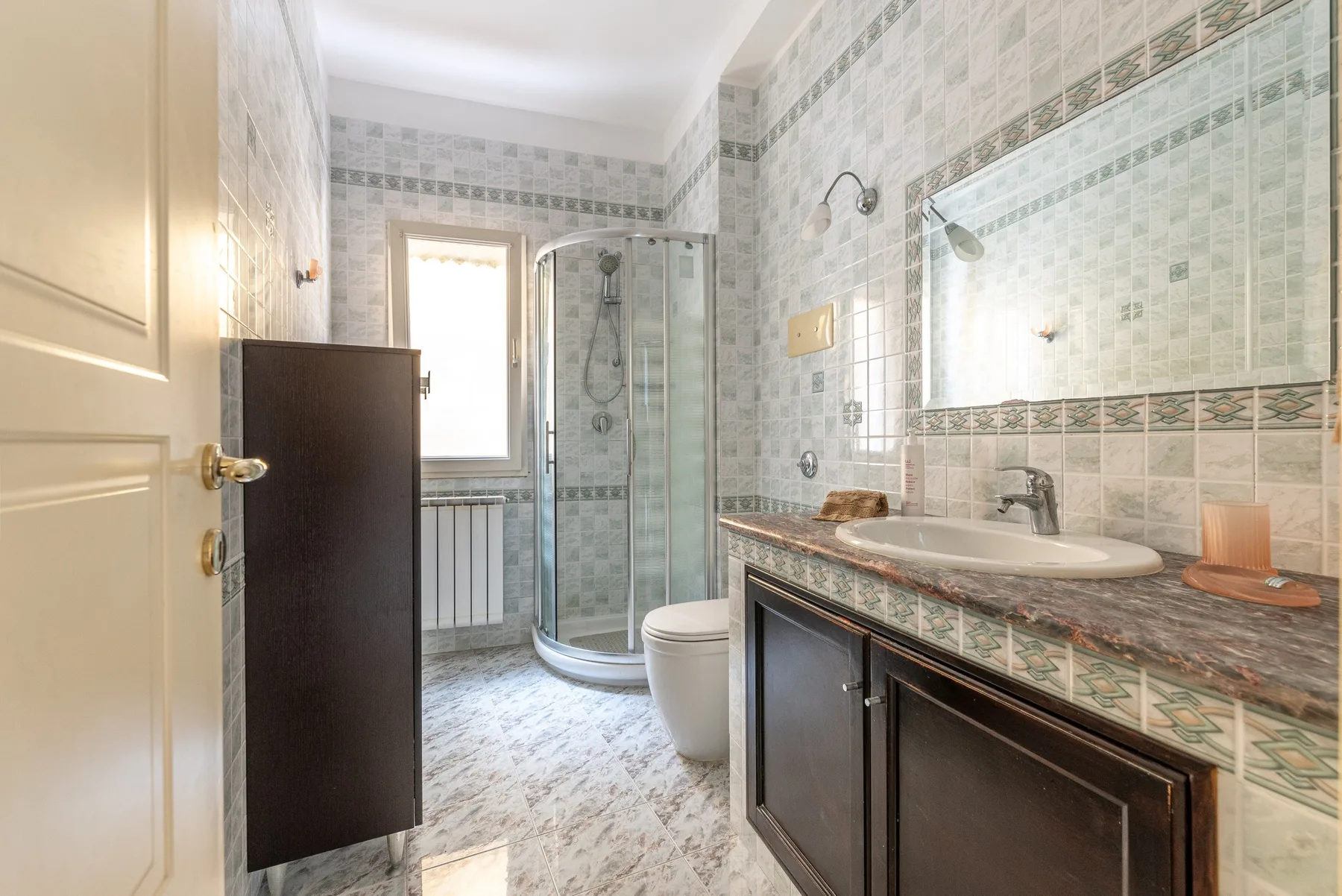 Un baño alicatado con ducha de vidrio, inodoro y lavabo.