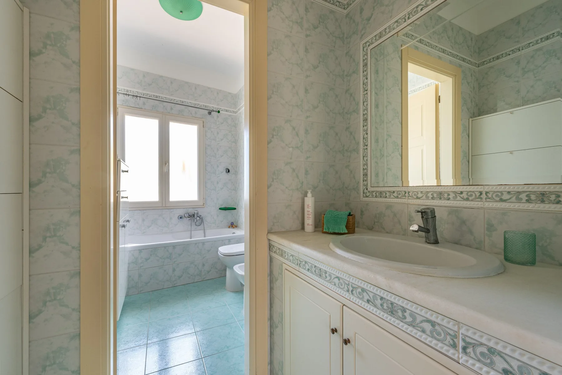 Un baño alicatado con bañera, tocador y un espejo grande en la pared.