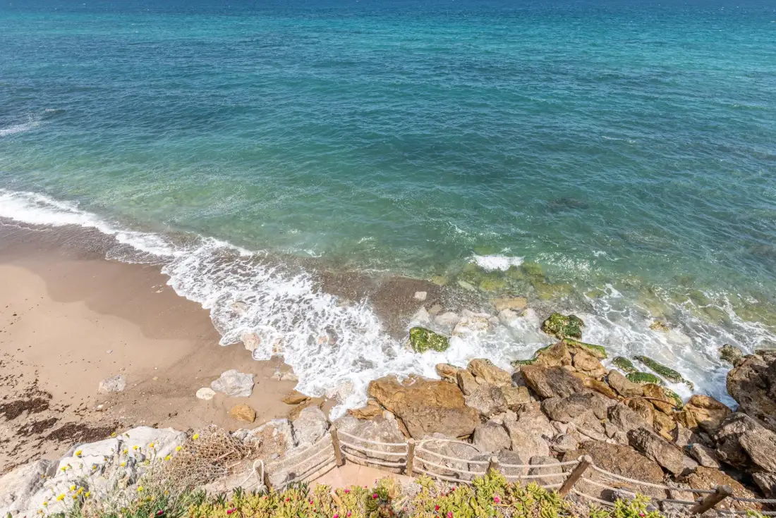 Una playa de arena se encuentra con agua turquesa junto a una costa rocosa.