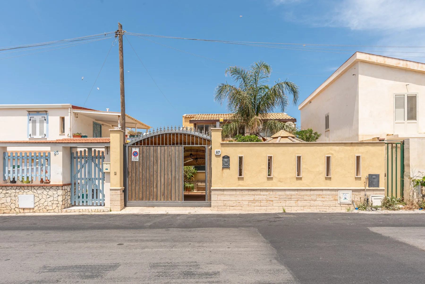 Una propiedad residencial frente a la calle, con entrada cerrada y una palmera.