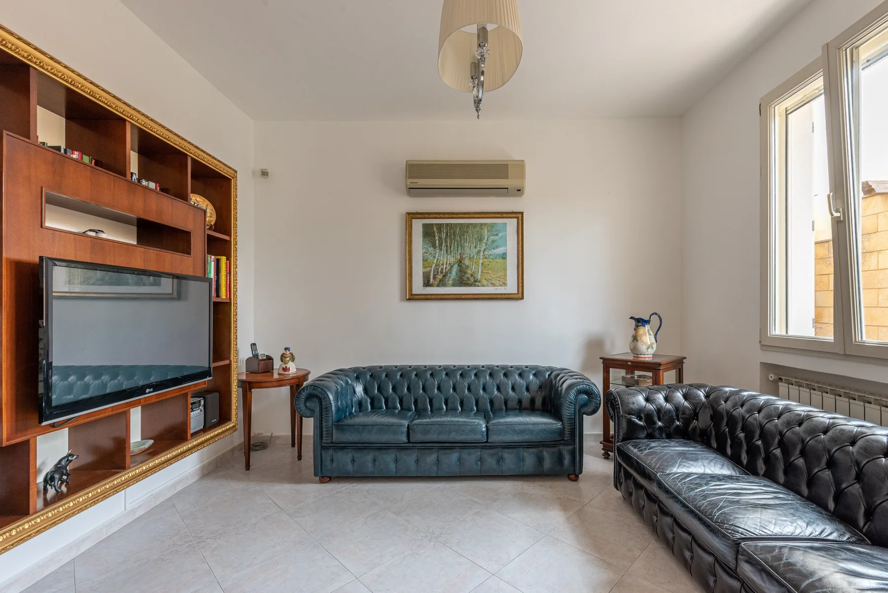 Una sala de estar con asientos capitoné, un televisor y grandes ventanas.