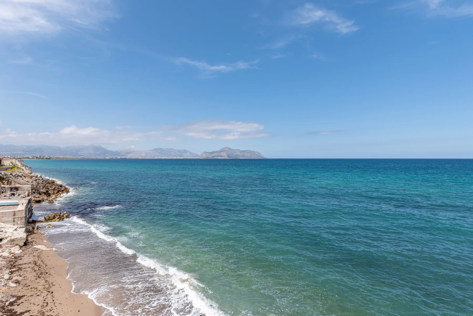 Una costa rocosa bordea una playa de arena junto al mar azul.