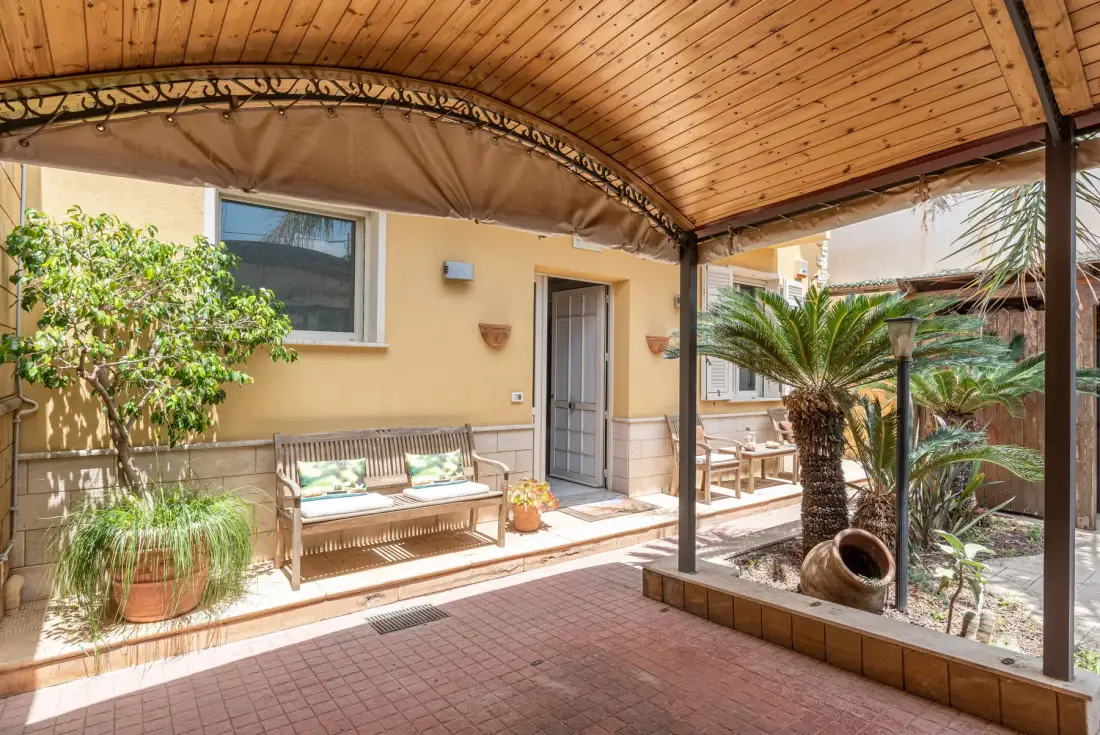 Un patio cubierto con asientos al aire libre, plantas en macetas y suelo de baldosas.