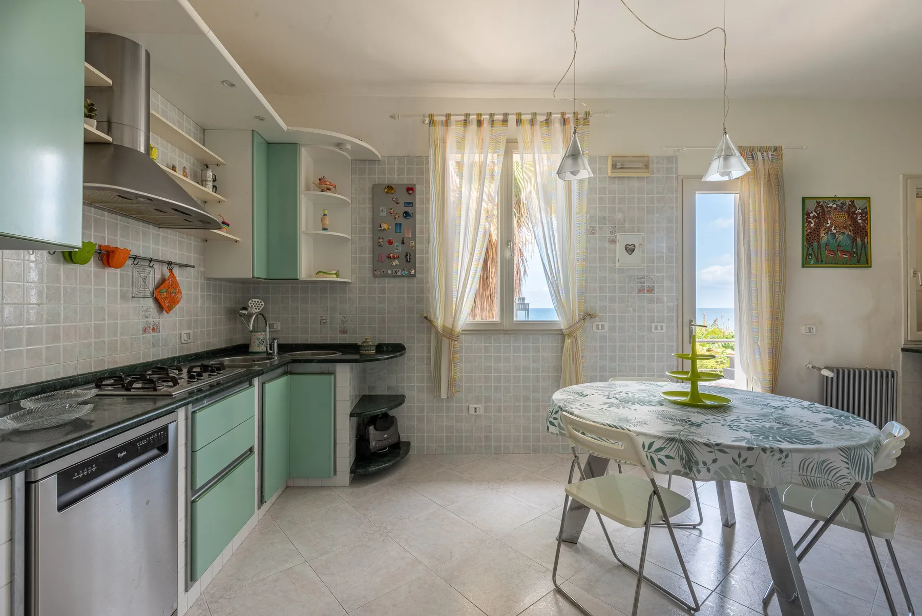 Una cocina con zona de comedor, armarios verdes y una mesa junto a las ventanas.