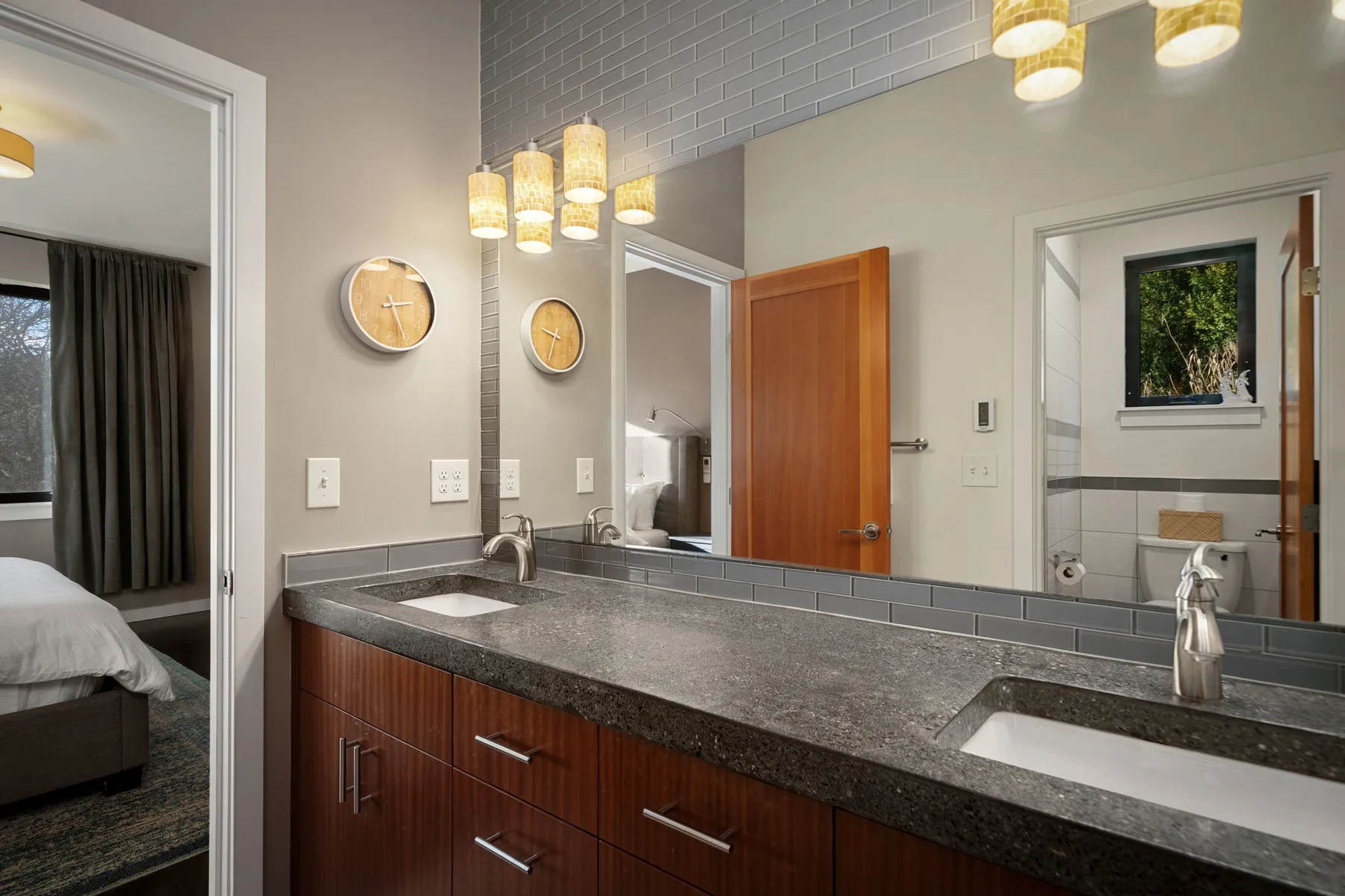 Un tocador de baño con dos lavabos, un espejo amplio y luces colgantes cálidas.