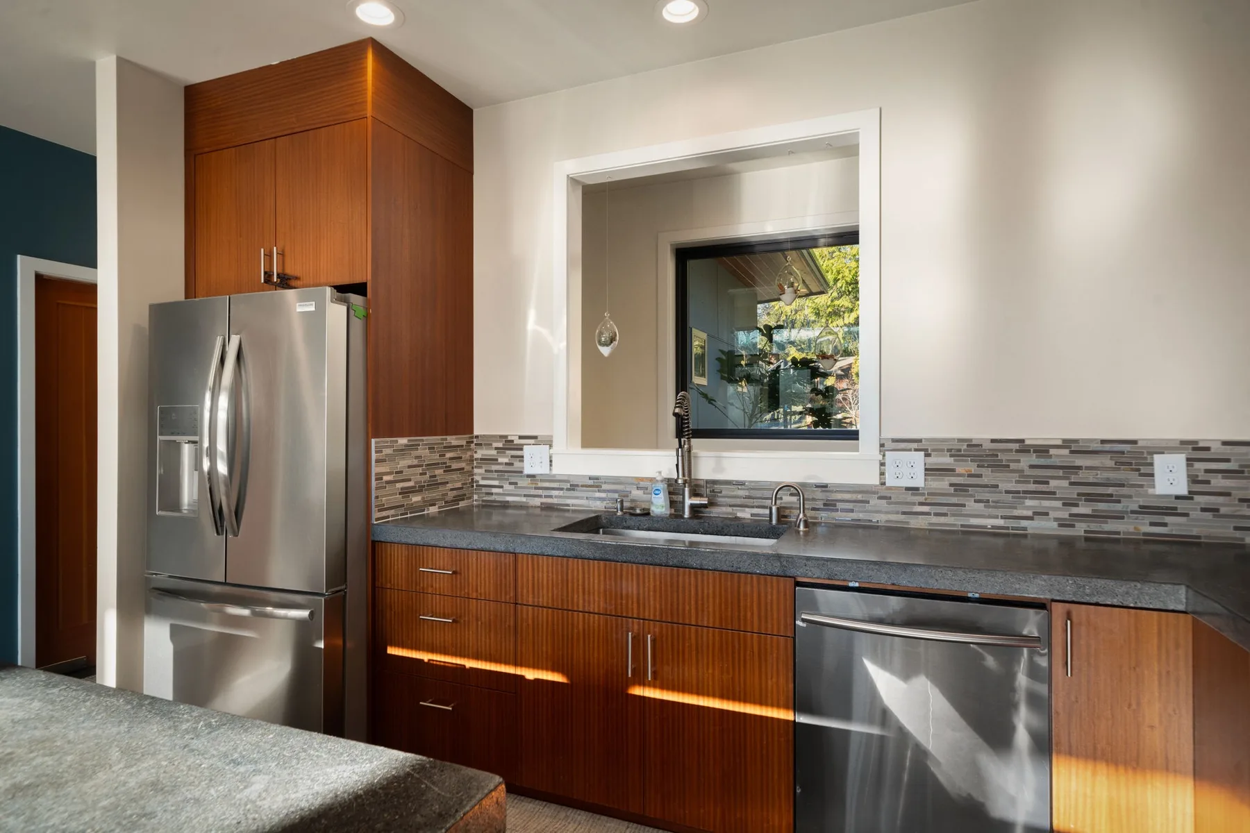 Una cocina moderna con gabinetes de madera, un refrigerador de acero inoxidable y una ventana sobre el fregadero.