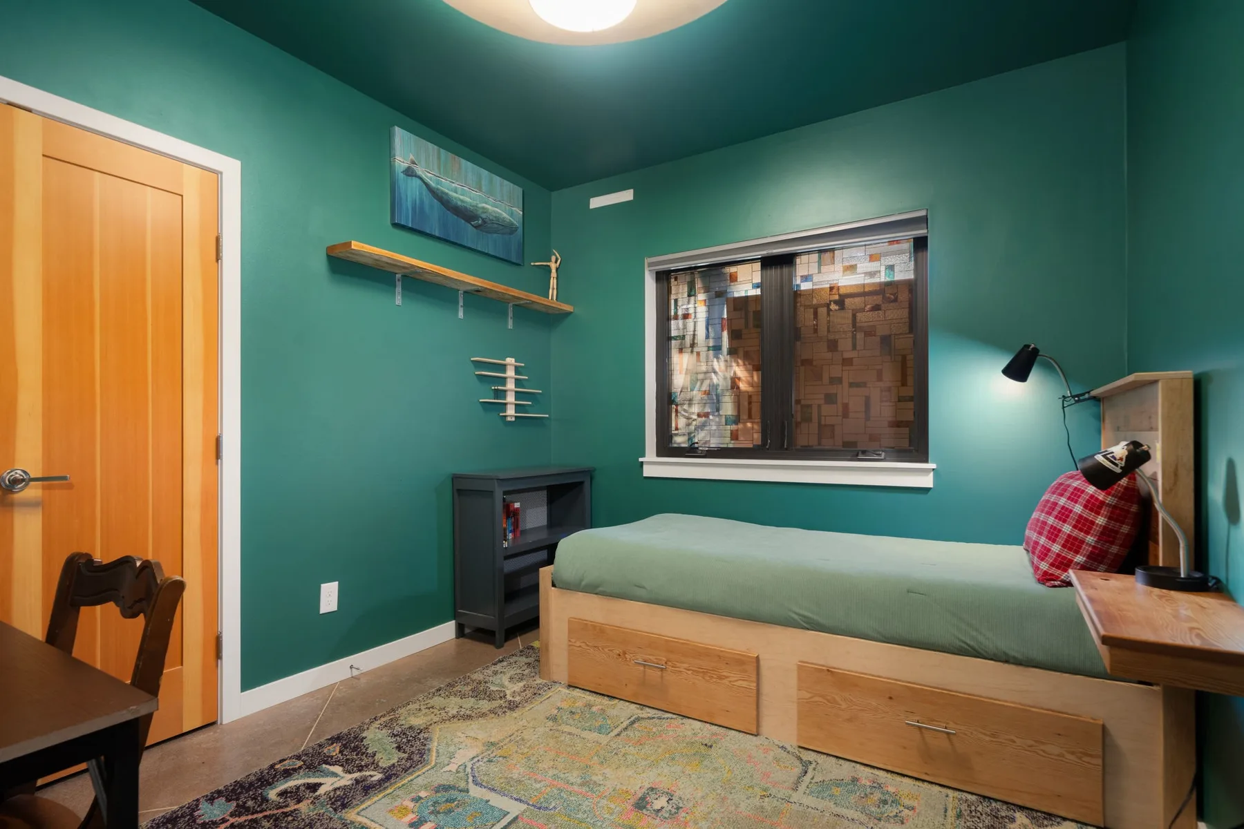 Un dormitorio con una cama, una ventana y paredes de color verde azulado.