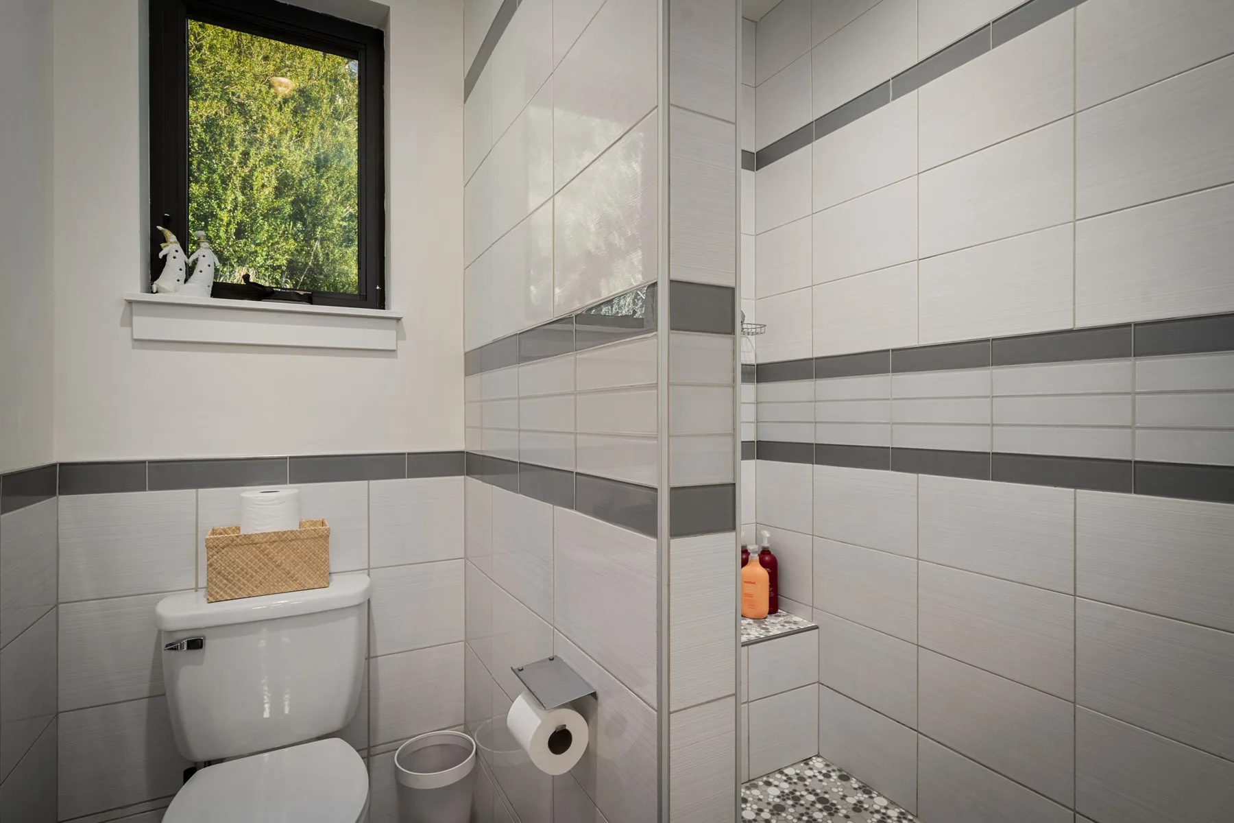 Un baño con azulejos, zona de ducha y una ventana con vistas a la vegetación.