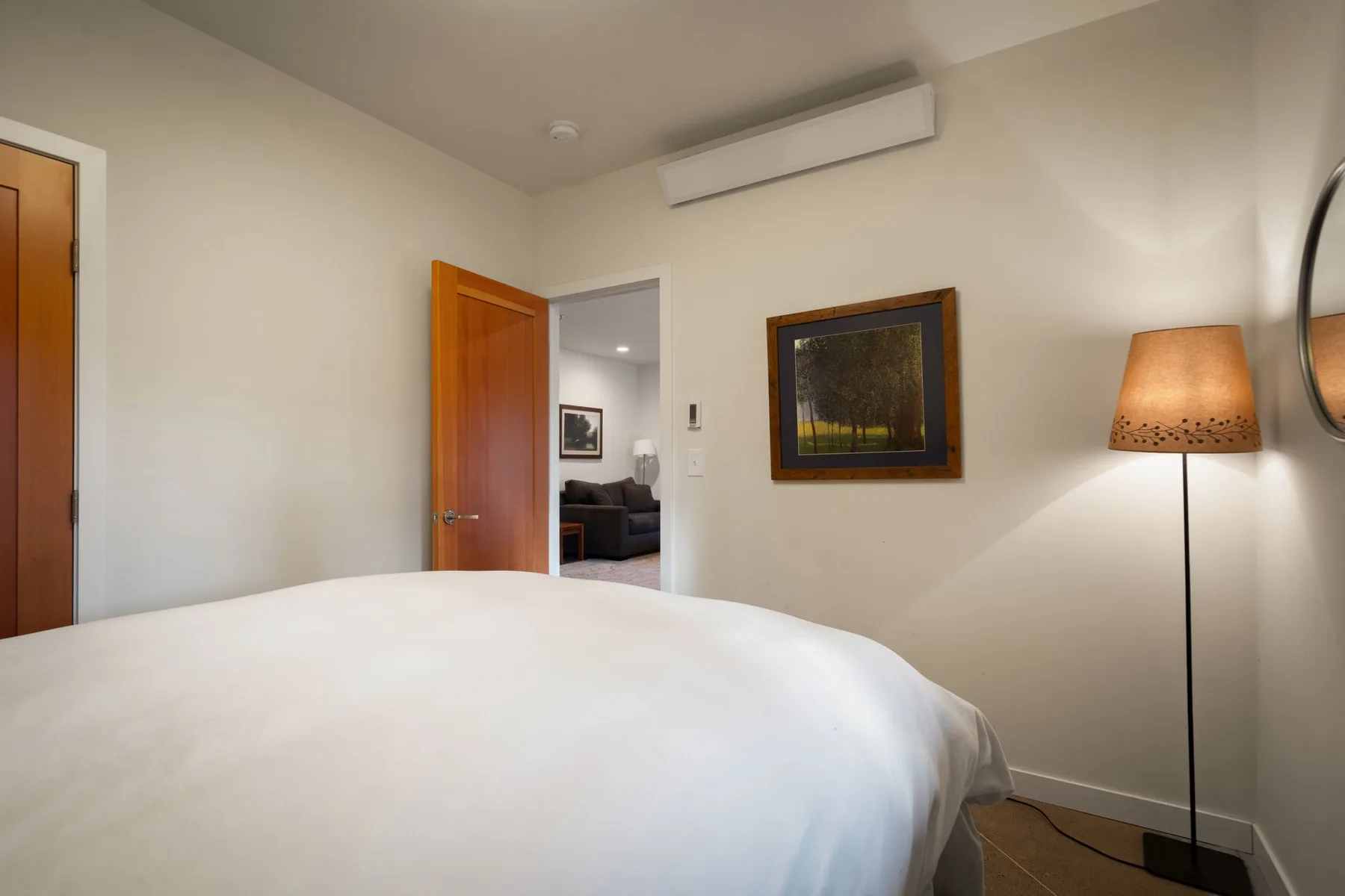 Un dormitorio con una cama blanca, arte en la pared y una lámpara de pie.