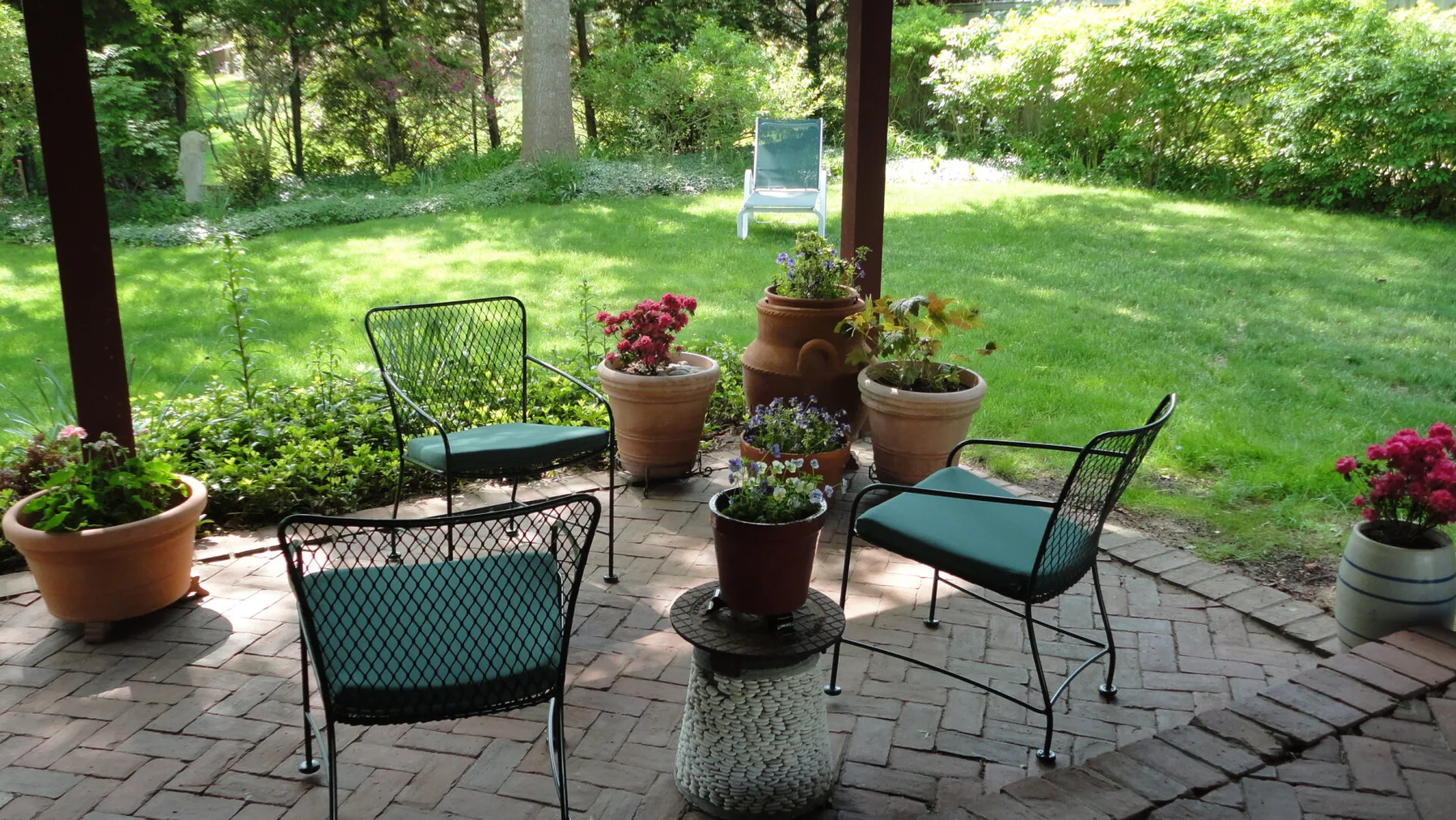 Un patio con asientos al aire libre y plantas en macetas da a un césped verde.