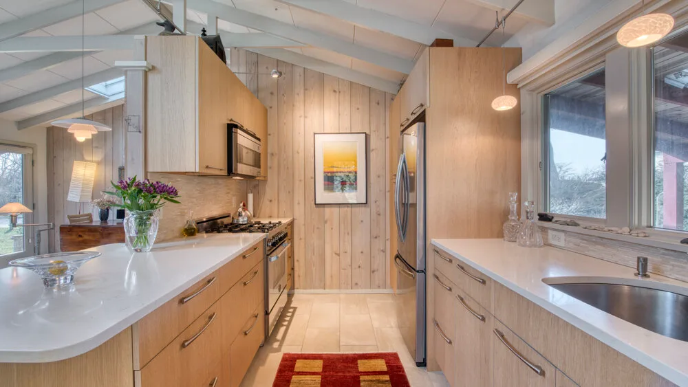 Una cocina luminosa con gabinetes de madera clara, amplias encimeras y un refrigerador central.