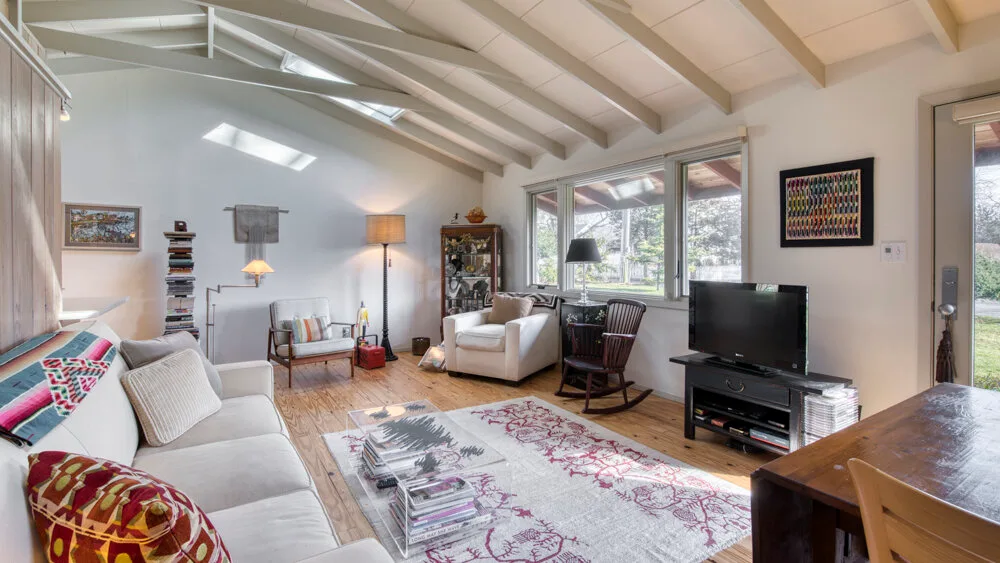 Una sala luminosa con asientos, una alfombra estampada y ventanas grandes.