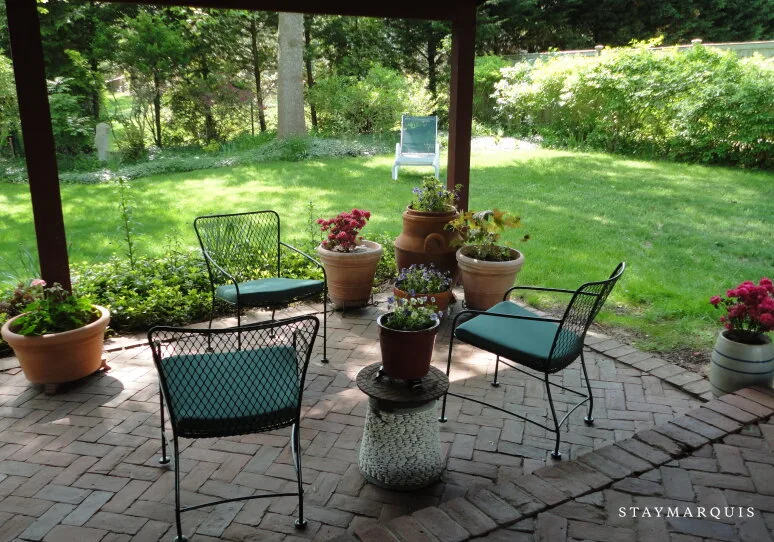 Un patio cubierto con asientos de exterior y plantas en macetas da a un césped verde.