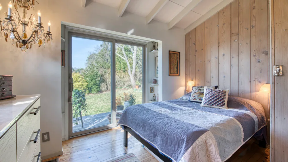 Un dormitorio con una cama junto a puertas corredizas de vidrio que dan a un jardín.