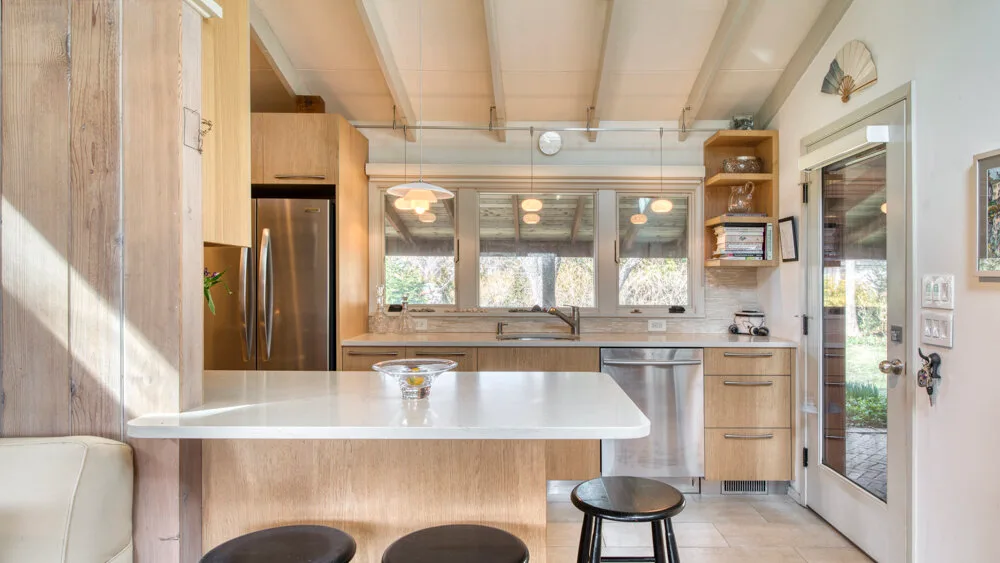 Una cocina luminosa con una isla central, taburetes y gabinetes de madera.