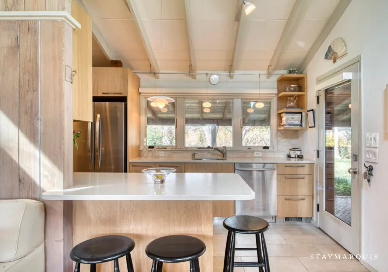 Una cocina luminosa con una isla central y ventanas sobre el fregadero.