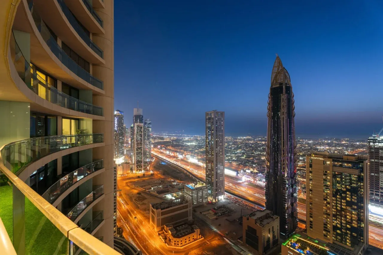 A balcony overlooks illuminated high-rise buildings and city streets at dusk.